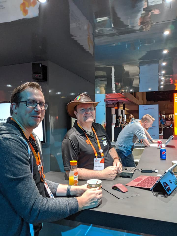 Two of us behind a conference booth counter, laptops open, mid-conversation with whoever walks up next