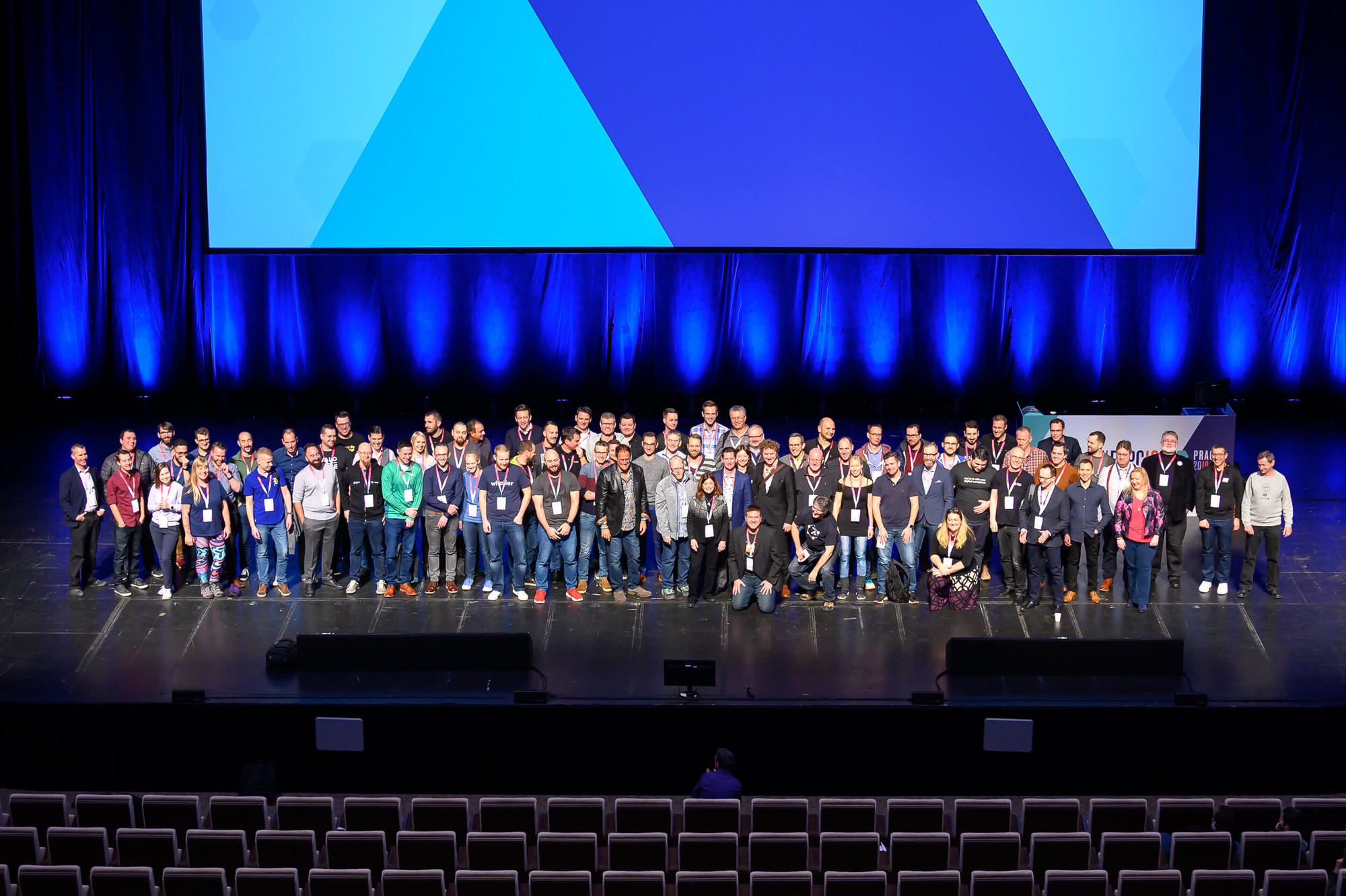 Around eighty speakers lined up across a conference stage for the traditional group photo, the empty auditorium in front of them