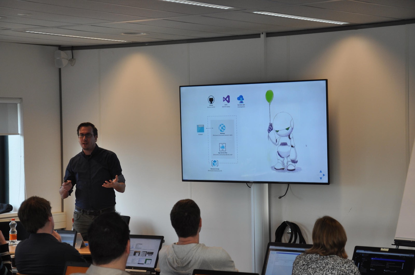 A speaker presenting an architecture diagram to a room of attendees working on laptops